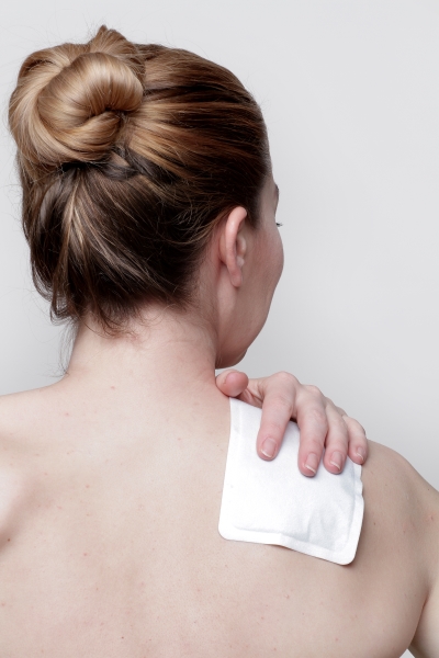 Frau nutzt ein Wärmepflaster zur Schmerzlinderung in der Schulter