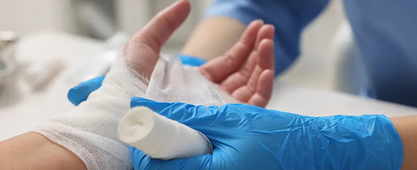Zinkleimverband Wirkung – Umwicklung Arzt mit Handschuhen wickelt Zinkleimverband für ideale Wirkung vorsichtig um die Hand des Patienten