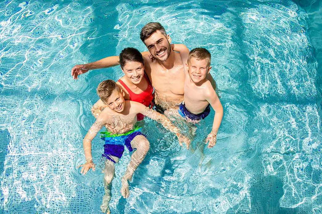 Suchen Sie bei großer Hitze Abkühlung – zum Beispiel im Schwimmbad Eine vierköpfige Familie kühlt sich in einem Swimmingpool ab